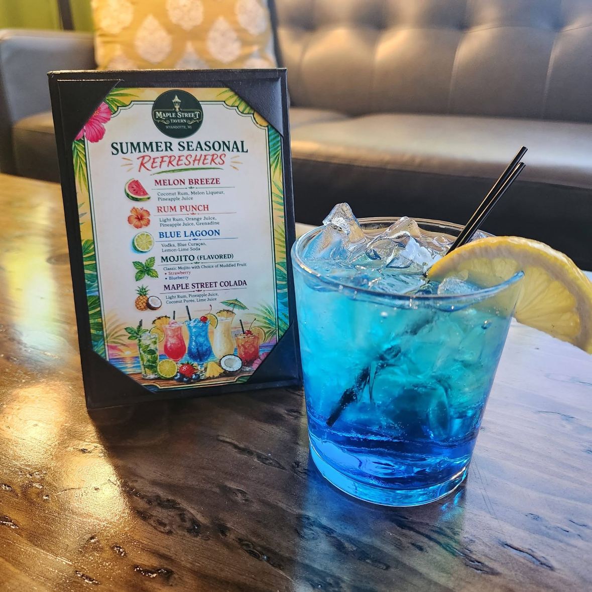 A Blue Lagoon cocktail on the bar next to the summer refreshers menu